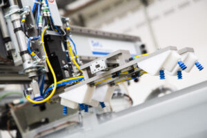 Ein Roboterarm mit blauen Saugnäpfen arbeitet in einer industriellen Umgebung voller Kabel.