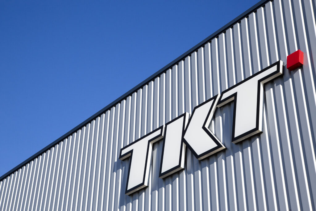 Gebäudefassade mit "TKT"-Schriftzug und rotem Würfel, vor klarem, blauem Himmel.