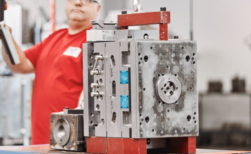 Industrielle Werkstatt mit großem metallischem Werkzeug, rotem Rahmen und Person im roten T-Shirt.